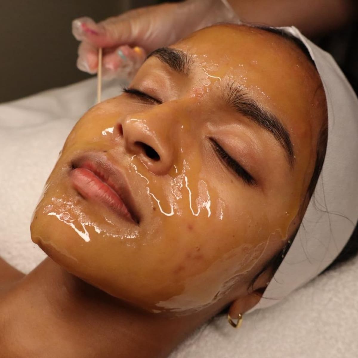 Woman lying with eyes closed as a glossy facial mask is applied during a spa treatment